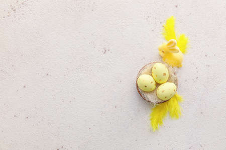 Bowl with painted Easter eggs, bunny and feathers on light background