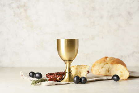 Cup of wine with bread and rosary on light background
