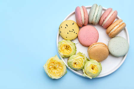 Plate with sweet macaroons and rose flowers on color background. International Women's Day...