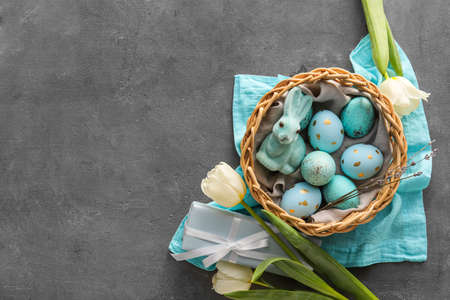 Basket with painted Easter eggs, bunny and tulip flowers on gray grunge background
