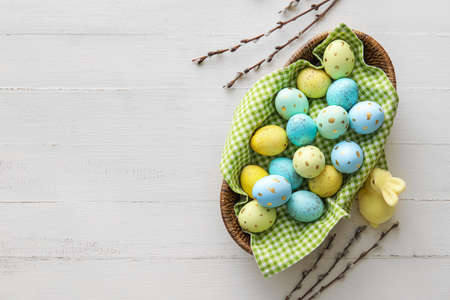 Basket with painted Easter eggs, willow branches and bunny on light wooden backgroundの写真素材