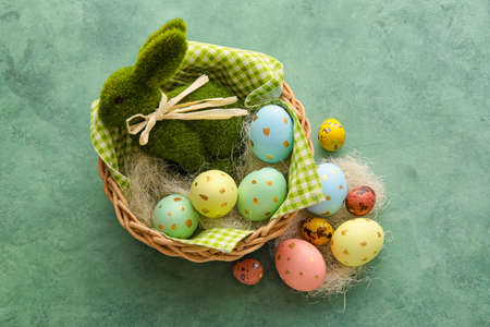 Basket with beautiful Easter eggs and bunny on green background