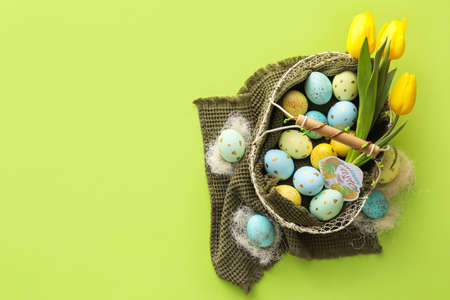 Basket with painted Easter eggs and tulip flowers on green background