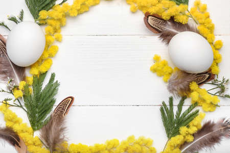 Easter wreath made of mimosa flowers, leaves, feathers and eggs on white wooden background, closeupの写真素材