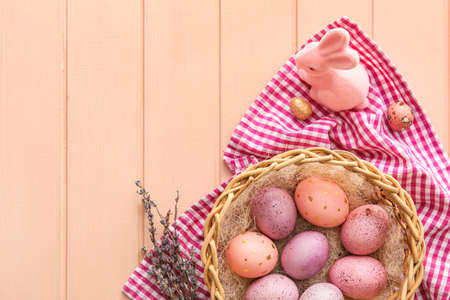 Basket with painted Easter eggs, lavender and bunny on pink wooden background