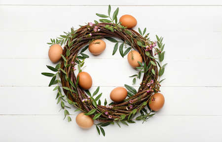 Easter wreath with eggs, flowers and leaves on white wooden background