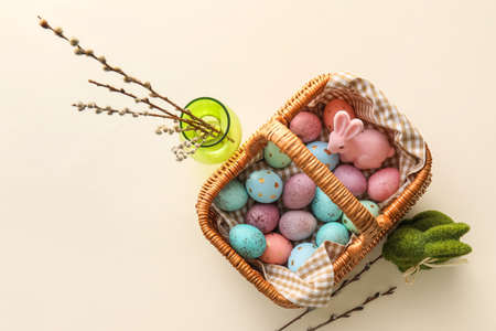 Basket with painted Easter eggs, willow branches and bunny on beige backgroundの写真素材