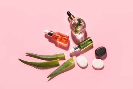 Composition with bottles of natural serum, spa stones and aloe leaves on pink backgroundの写真素材