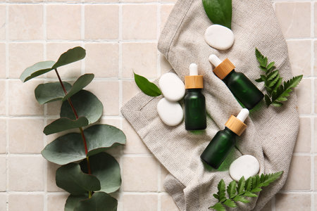 Composition with bottles of natural serum, spa stones and eucalyptus branch on light tileの写真素材