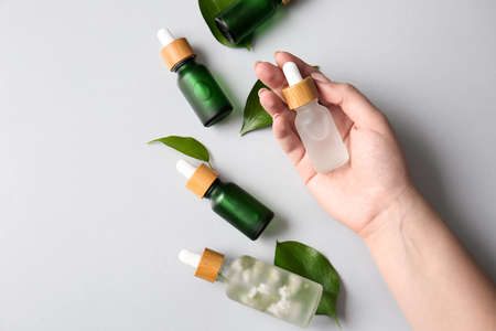 Female hand with bottles of natural serum and plant leaves on white background, closeupの写真素材