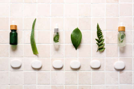 Composition with bottles of serum, plant leaves and spa stones on light tile
