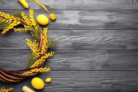 Composition with Easter wreath, eggs and mimosa flowers on gray wooden background
