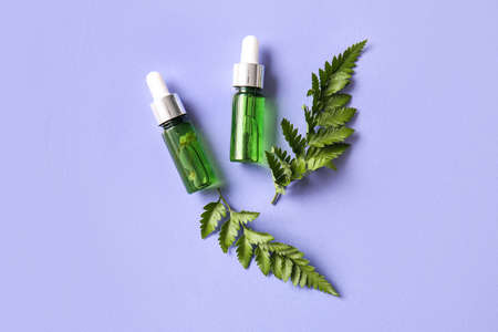 Bottles of natural serum and fern leaves on lilac backgroundの写真素材