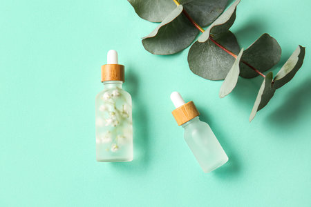 Bottles of natural serum and eucalyptus branch on color backgroundの写真素材