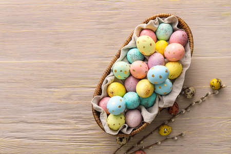 Basket with painted Easter eggs and willow branches on wooden background