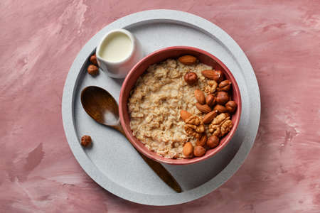 Bowl of tasty oatmeal with nuts on pink backgroundの写真素材