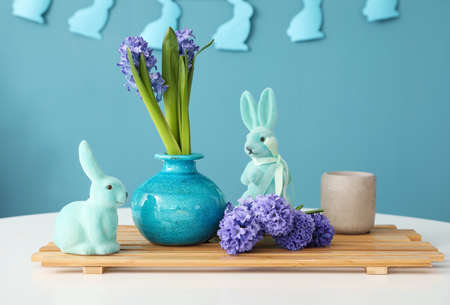 Vase with beautiful hyacinth flowers and Easter bunnies on table against blue backgroundの写真素材