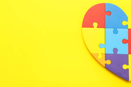 Heart made of colorful puzzle pieces on yellow background. Concept of autistic disorderの写真素材