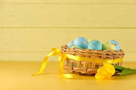 Wicker basket of painted Easter eggs and flowers on yellow backgroundの写真素材