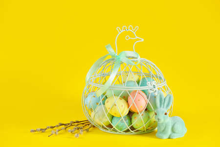Basket of painted Easter eggs, pussy willow and toy bunny on yellow background