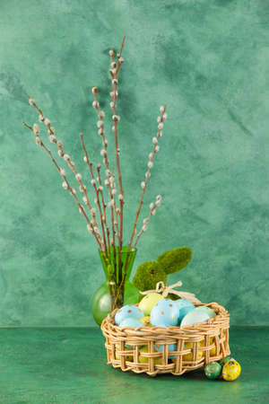 Wicker basket of painted Easter eggs, pussy willow and toy bunny on green background