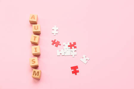 Cubes with word AUTISM and puzzle pieces on pink background