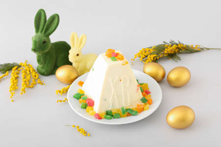 Traditional curd Easter cake with candied fruits, golden eggs, bunnies and mimosa flowers on light...