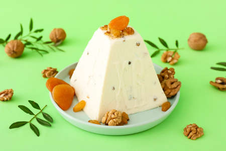 Plate with curd Easter cake, walnuts and dried apricots on green background