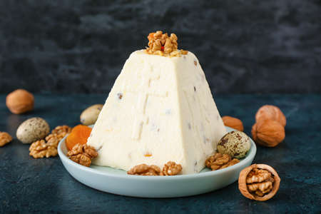 Plate with tasty curd Easter cake and walnuts on dark background