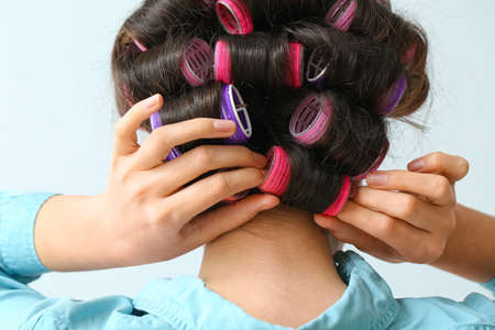 Beautiful young woman in hair rollers on light background, closeupの写真素材