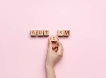 Female hand and wooden cubes with word AUTISM on pink backgroundの写真素材