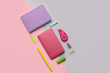 Different stationery supplies on pink and gray background
