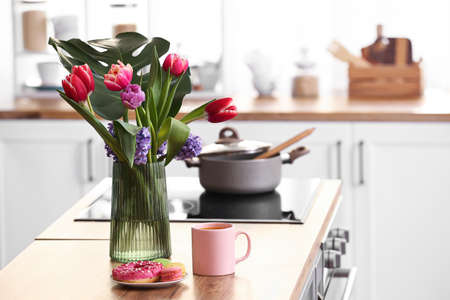 Vase with flowers and delicious breakfast on kitchen counter