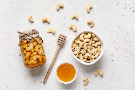 Jar of tasty cashew nuts with honey and dipper on light backgroundの写真素材