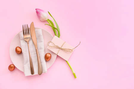 Beautiful table setting with Easter eggs and tulip on pink background