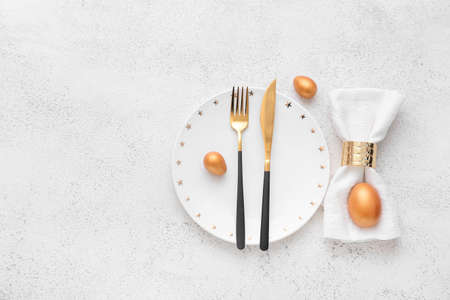 Beautiful table setting with golden Easter eggs on white background