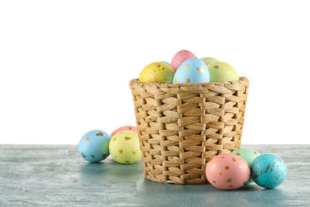 Wicker basket of painted Easter eggs on table against white background