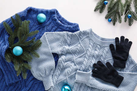 Knitted sweaters, gloves and Christmas decor on light background