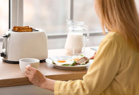 Mature woman eating tasty toasts and drinking coffee in kitchen