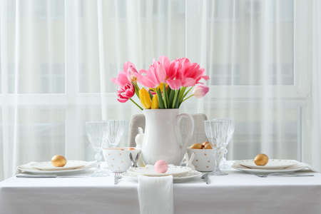Beautiful table setting with Easter eggs and tulips in roomの写真素材