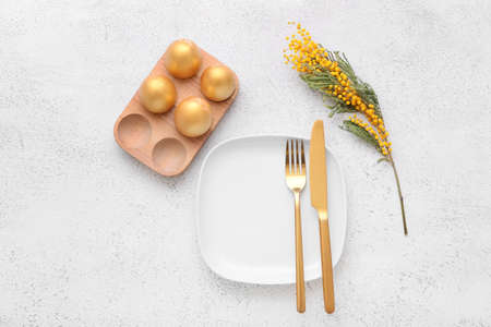 Beautiful table setting with Easter eggs and mimosa flowers on white background