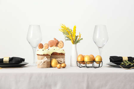 Beautiful Easter table setting with mimosa flowers near light wall