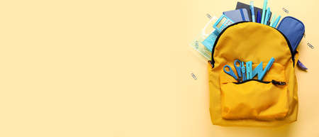 School backpack and stationery on yellow background with space for text
