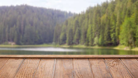 Empty wooden table near lake in coniferous forest. Mockup for design