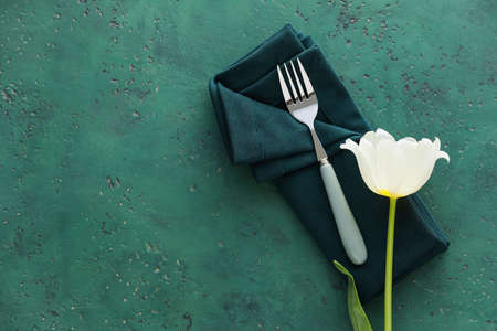 Fork, napkin and white tulip on green background