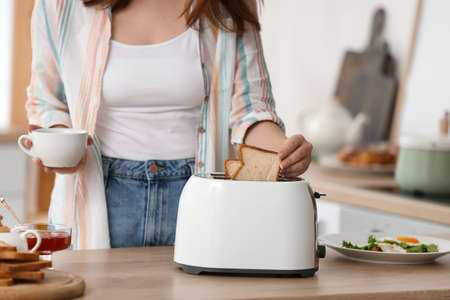 Beautiful young Asian woman drinking coffee and making tasty toasts in the kitchenの写真素材