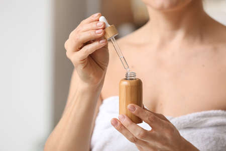 Mature woman using cosmetic serum in bathroom, closeup