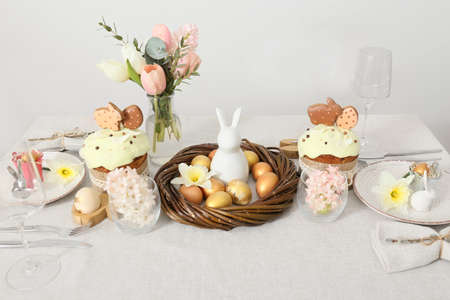 Beautiful Easter table setting with flowers near light wall