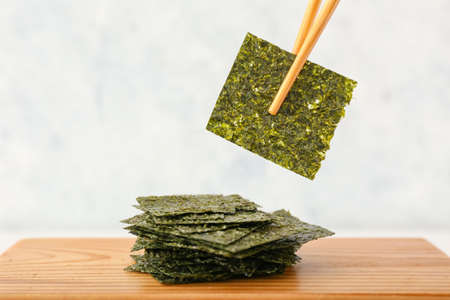 Wooden board with tasty seaweed sheets on light background