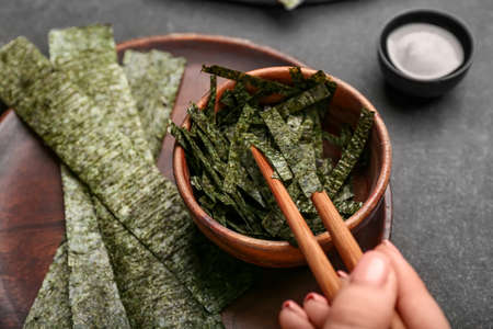 Woman eating tasty seaweed sheets on black background, closeupの写真素材